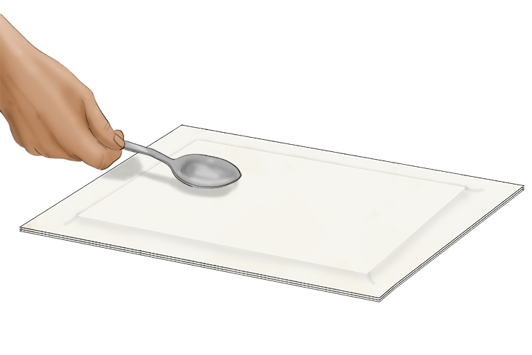 Holding the paper in place to stop it from moving, use the back of a spoon in circular motions to press the board onto the paper.